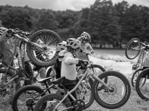 Black and white image. Children, in a forest trail, are lining up their mountain bikes pointing to the right. Anticipating next instruction.