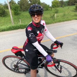 Tracey Band posing on her bicycle in full road cycling kit, sunglasses and helmet
