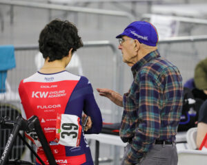 Manuel Avelar, wearing dress shirt and pants, and cycling cap discussing race tactics with his grandson in full racing kit