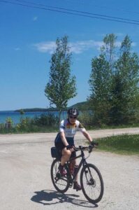 Woman cyclist on gravel road, clear skies and waterfront background