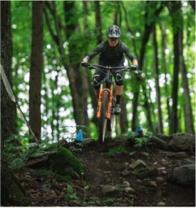 woman cresting a hill in the forest on her mountain bike