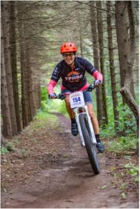 Woman cyclist on her mountain bike through a forest trail smiling at the camera