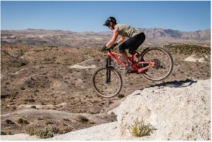 Woman cyclist jumping off a rock with the desert in the background