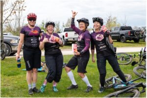 4 women in their mountain bike exchange jerseys and helmets smiling and posing with their arms in the air