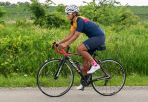 Woman in full cycling kit, road cycling with a grassy field behind