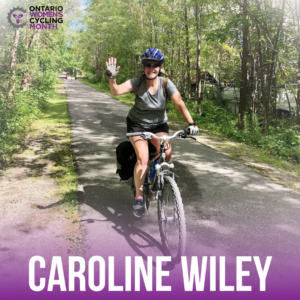 photo taken of a female cyclist in a tree lined pathway, smiling and waving at the camera, Text reads Caroline Wiley