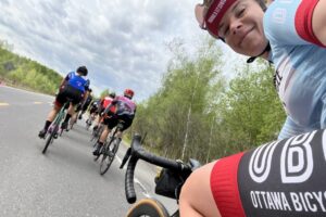 an OBC cyclist selfie from the back of the peloton showcasing her smile and the group ride ahead